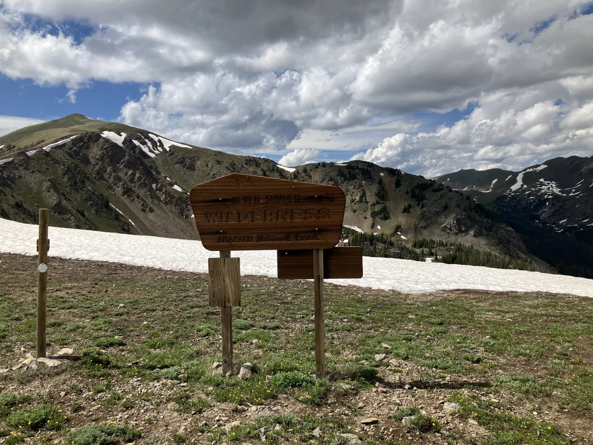 Never Summer Wilderness boundary sign above Bowen Lake with forested mountains in Arapaho National Forest, Colorado